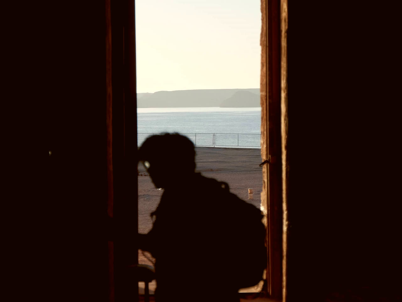 La silueta de una persona de pie en el umbral de una puerta abierta; al otro lado, el mar y la luz tenue de la mañana.